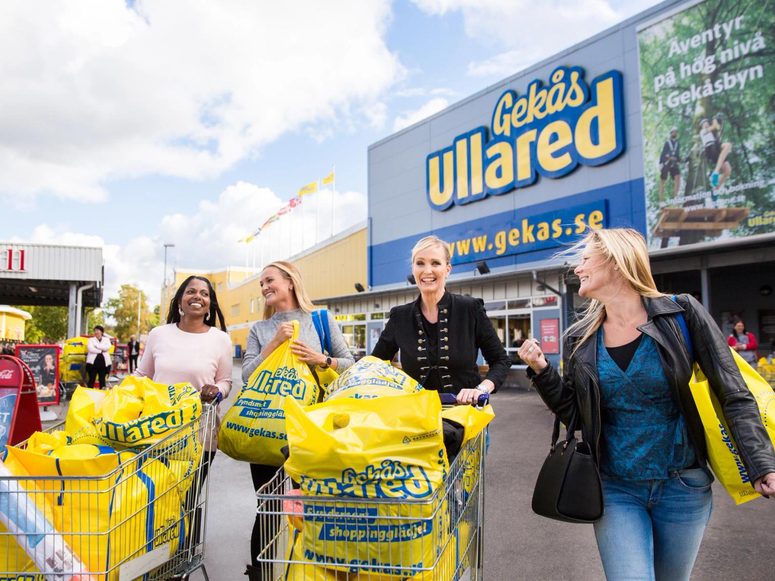 tre kvinder skubber indkøbsvogne fulde af gule poser foran en butik