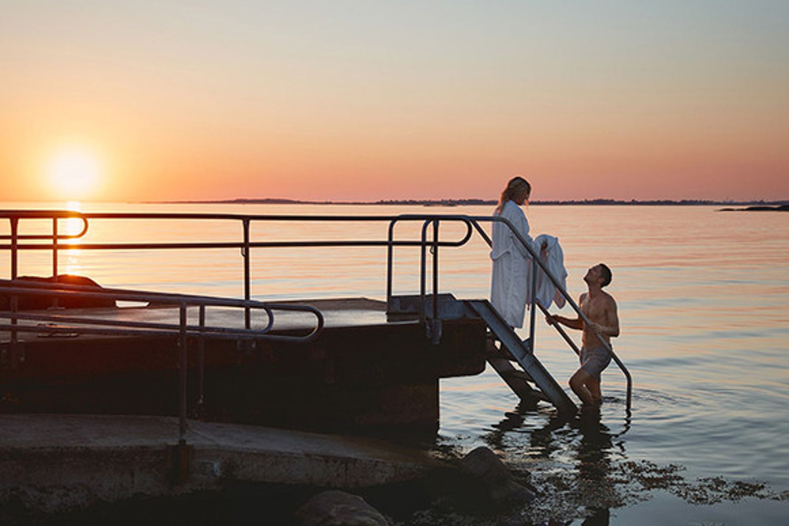 en man och en kvinna står på en brygga i vattnet vid solnedgången
