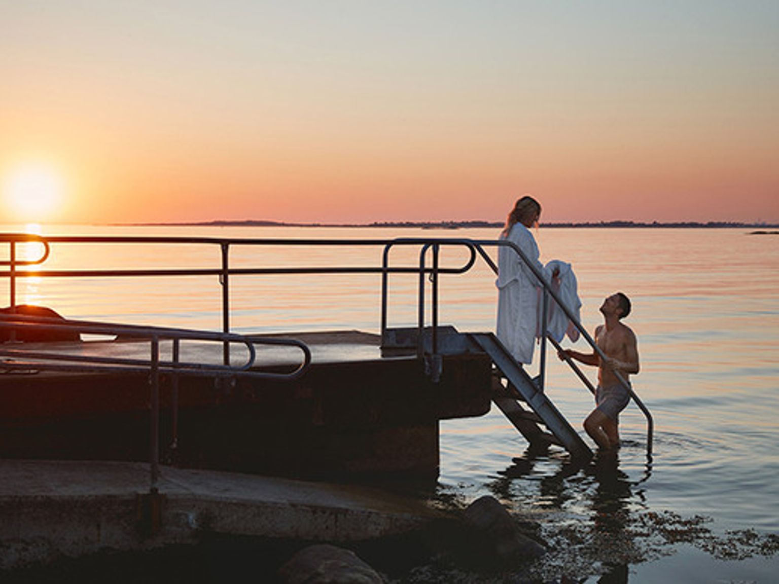 en mann og en kvinne står på en brygge i vannet ved solnedgang
