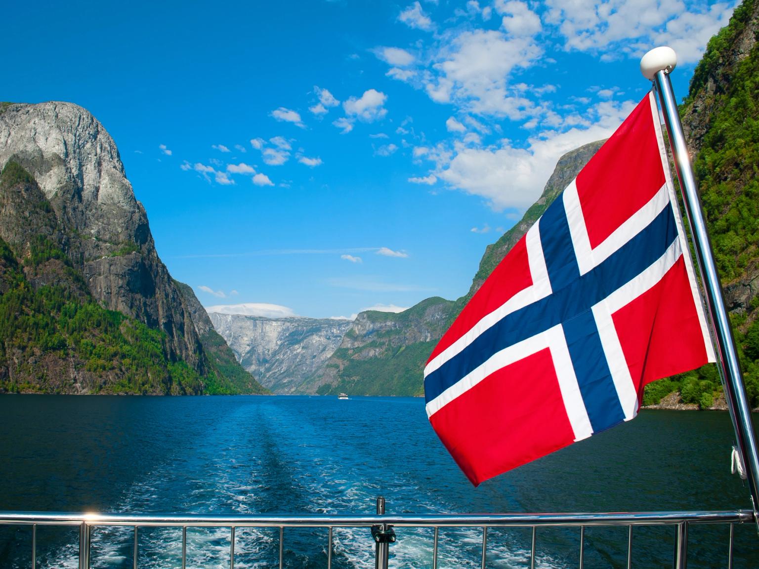 una bandera noruega vuela sobre un lago con montañas en el fondo