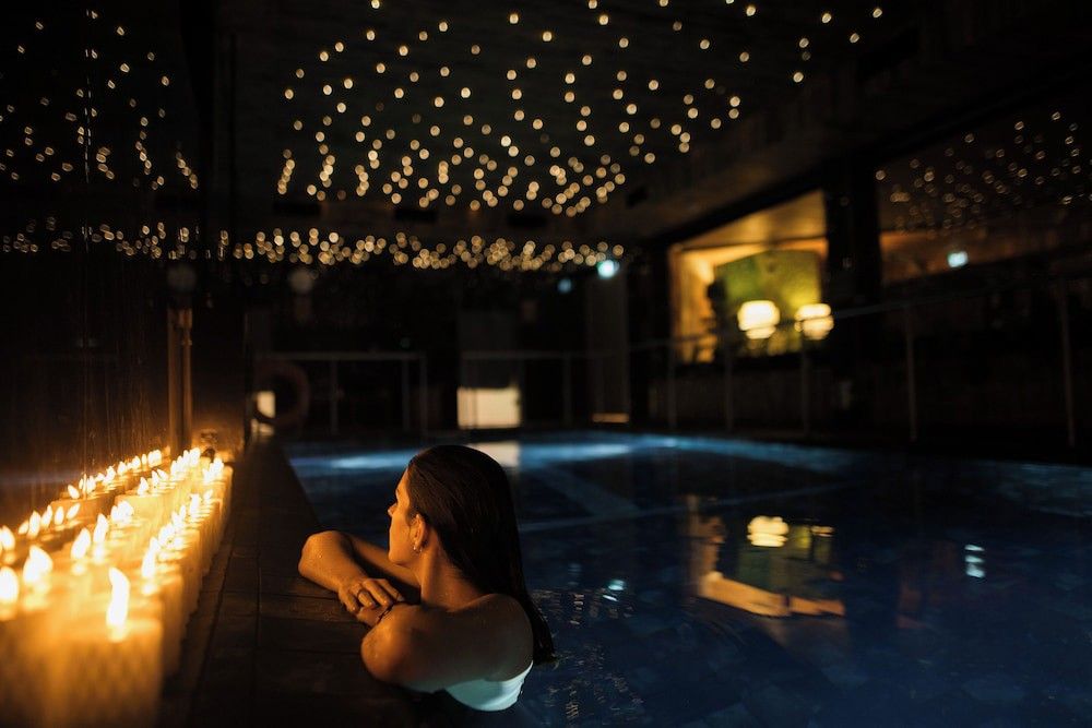 Kvinna i en ljusupplyst inomhuspool under en stjärnbeströdd tak. Aito Igloo & Spa Resort