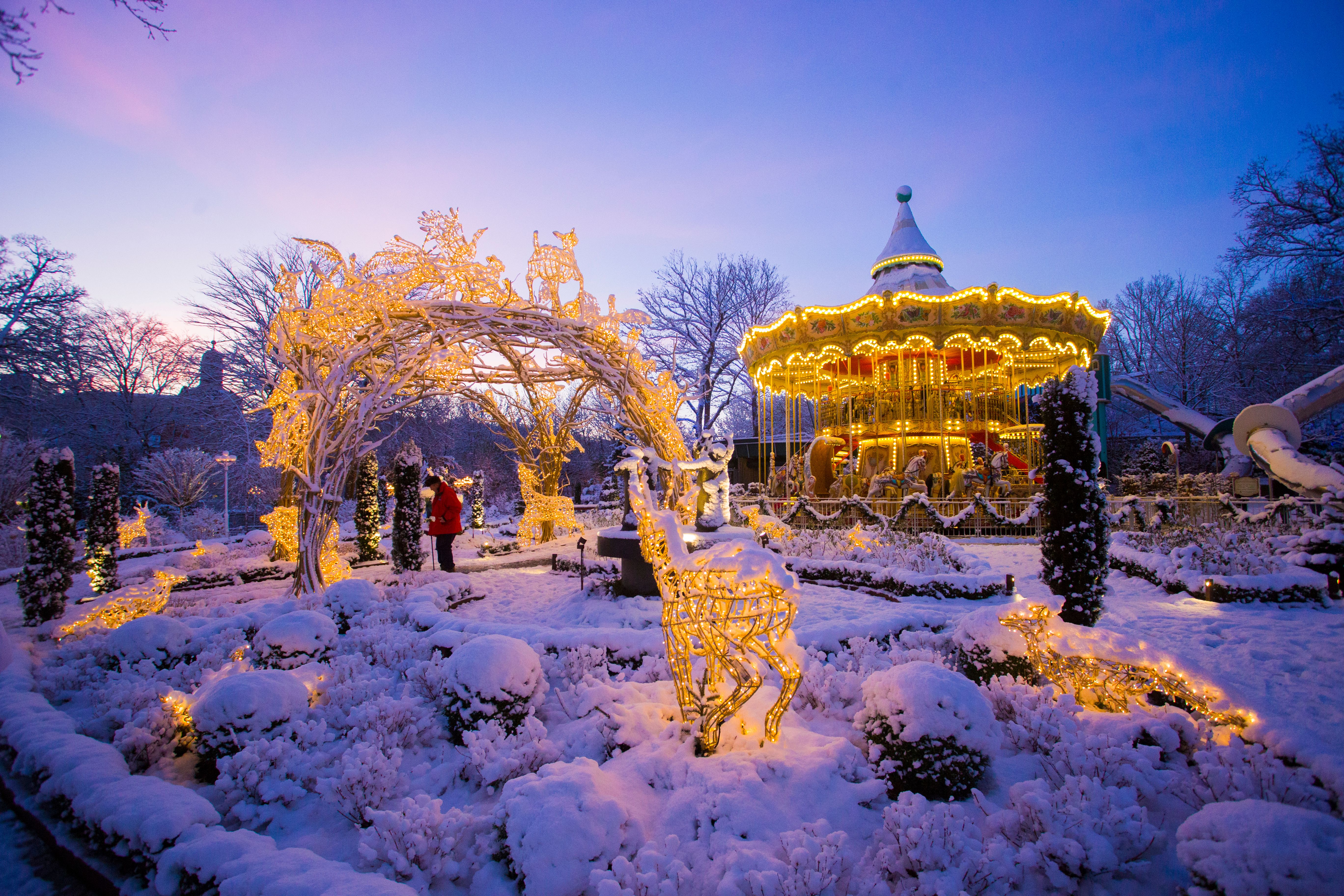 Snesækket park i skumringen med en stærkt oplyst karrusel og glitrende juledekorationer.