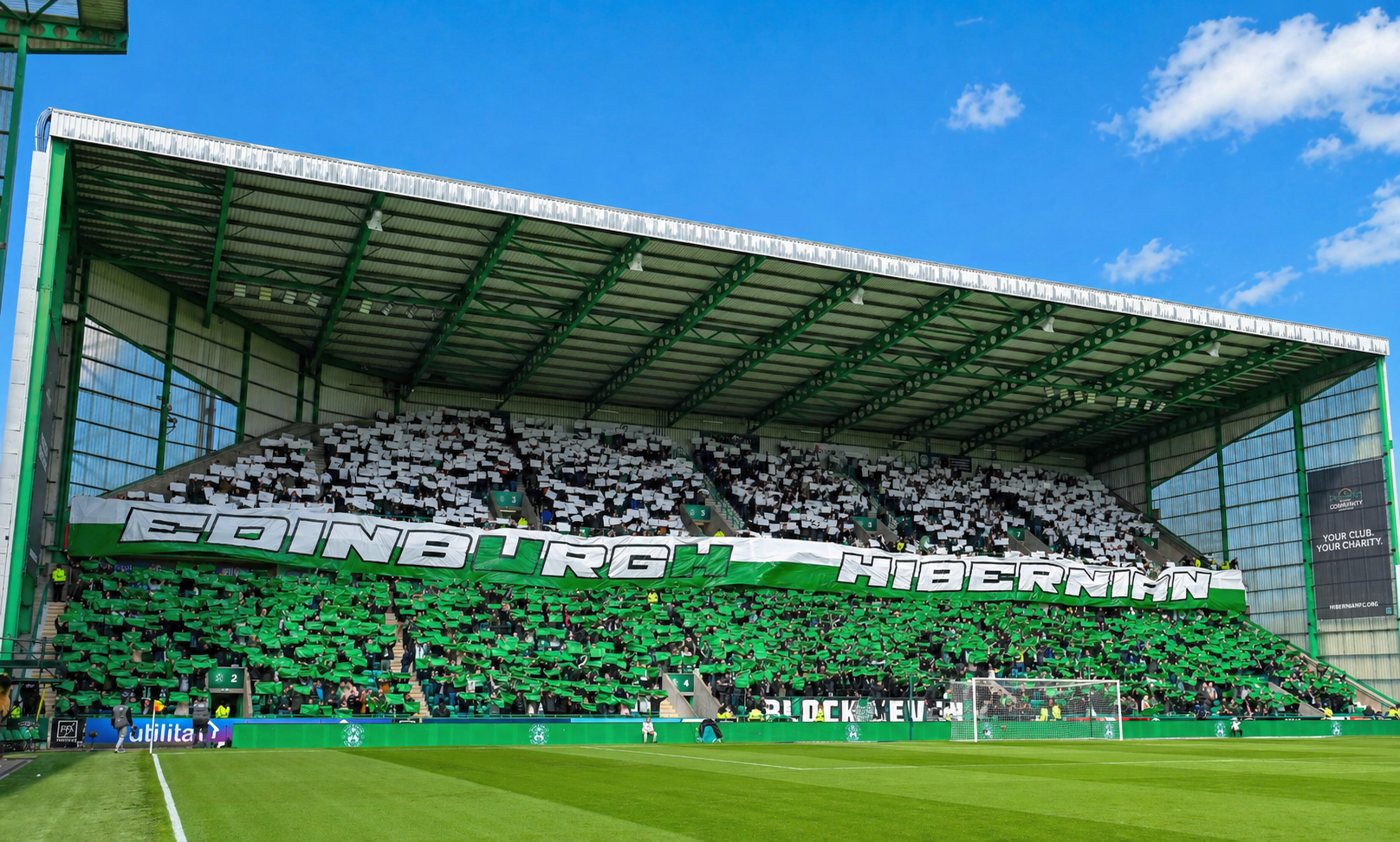 Football fans in a stadium stand create a green and white card display with a banner reading "EDINBURGH HIBERNIAN."
