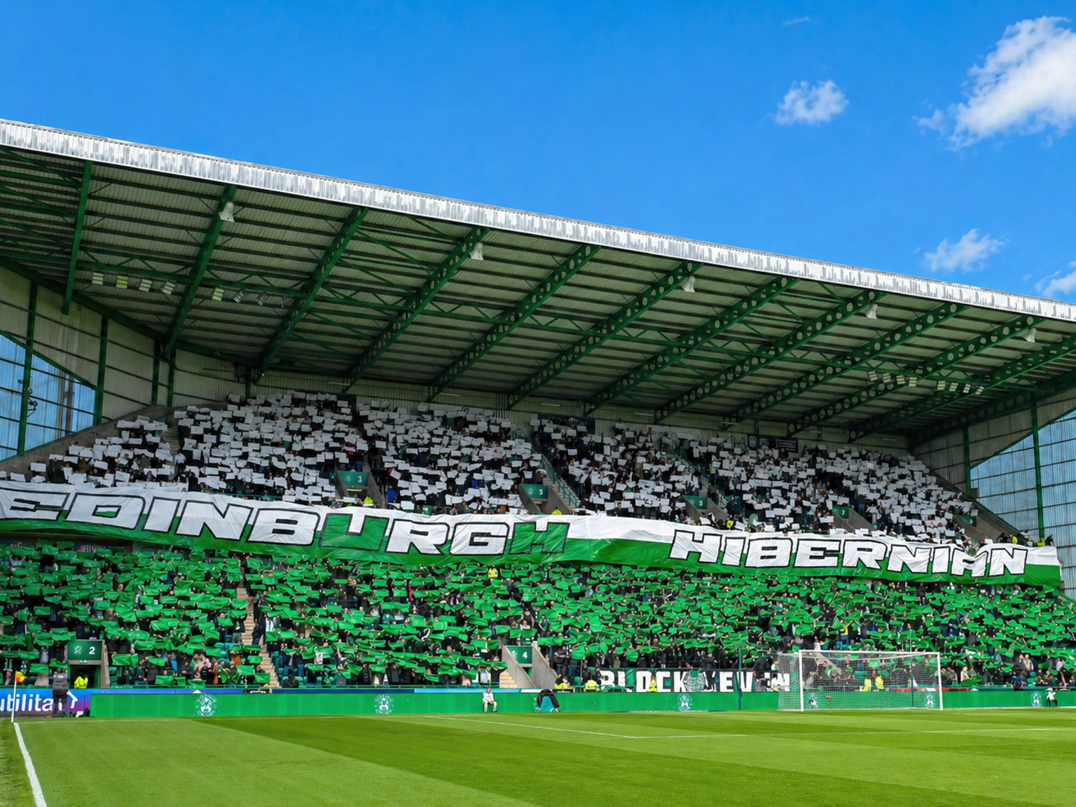 Football fans in a stadium stand create a green and white card display with a banner reading "EDINBURGH HIBERNIAN."
