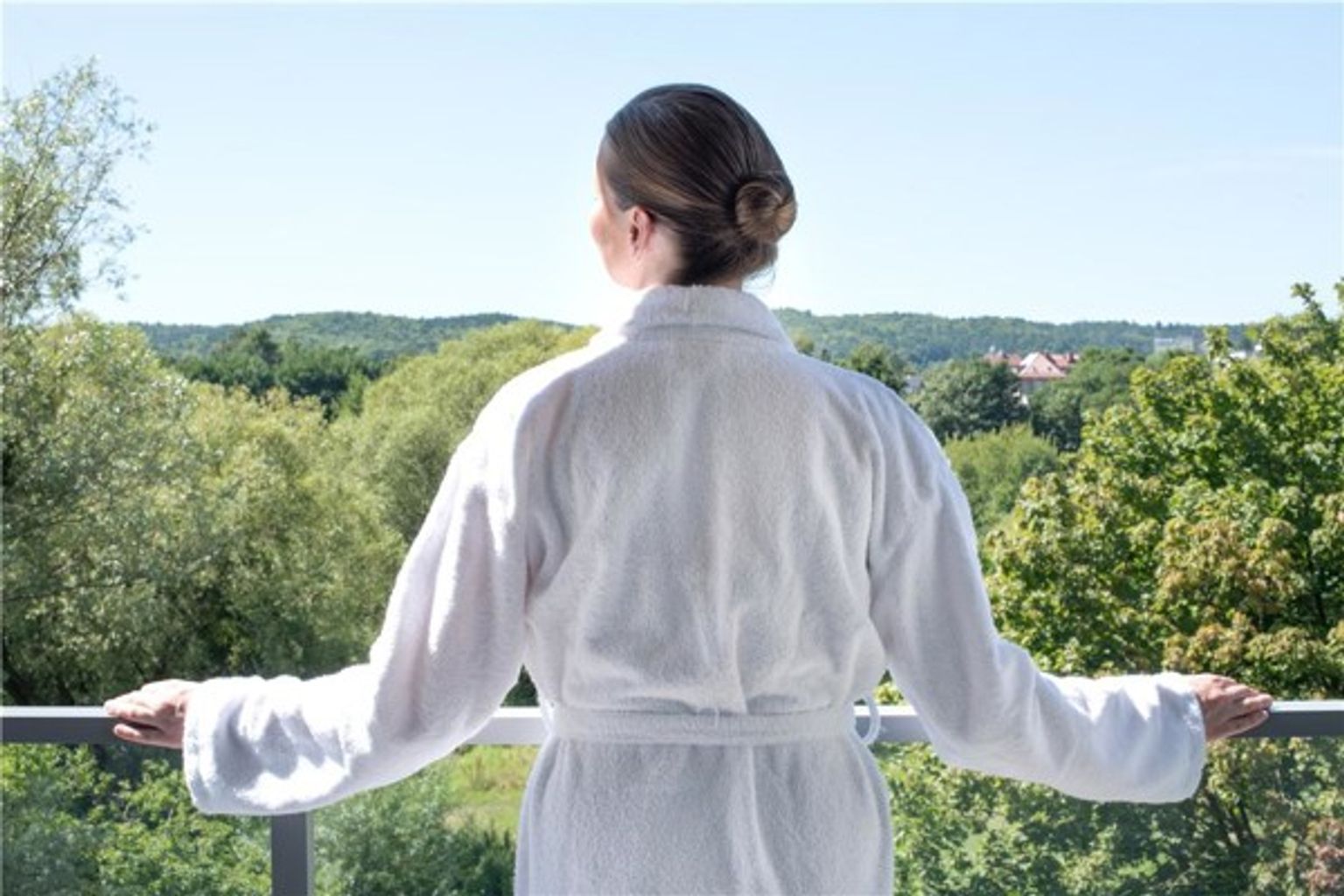en kvinna i en badrock står på en balkong och tittar ut över en skog.