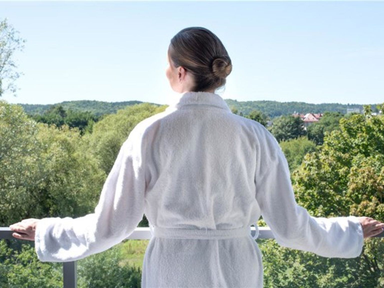en kvinna i en badrock står på en balkong och tittar ut över en skog.