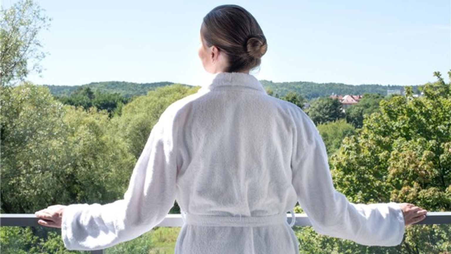 en kvinna i en badrock står på en balkong och tittar ut över en skog.