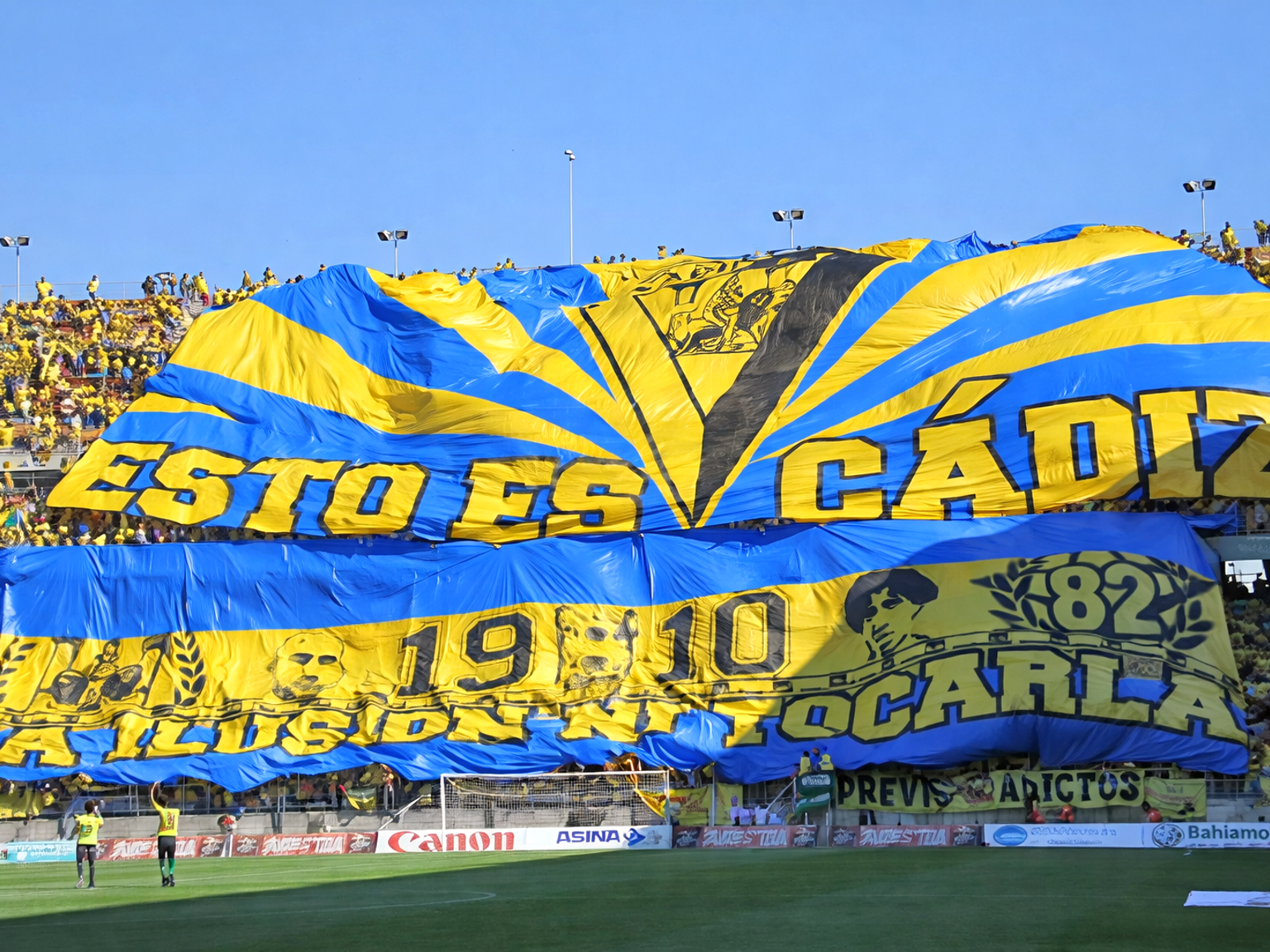 Um grande tifo azul e amarelo com a frase "ESTO ES CÁDIZ" estendido sobre uma multidão de torcedores de futebol em um estádio.