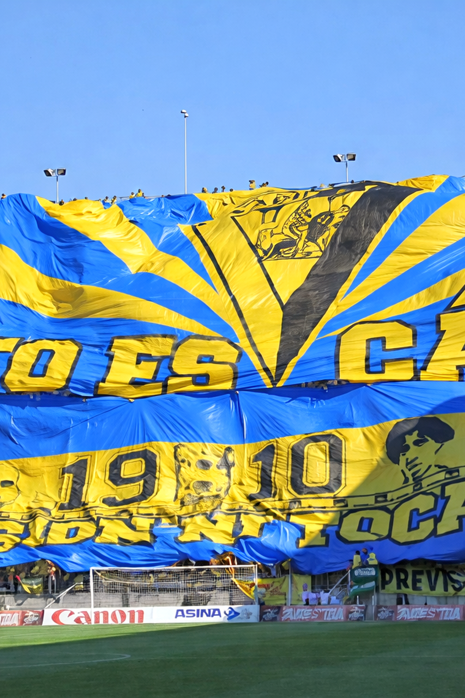 Et stort blåt og gult tifo med teksten "ESTO ES CÁDIZ" rullet ud over en menneskemængde af fodboldfans på et stadion.