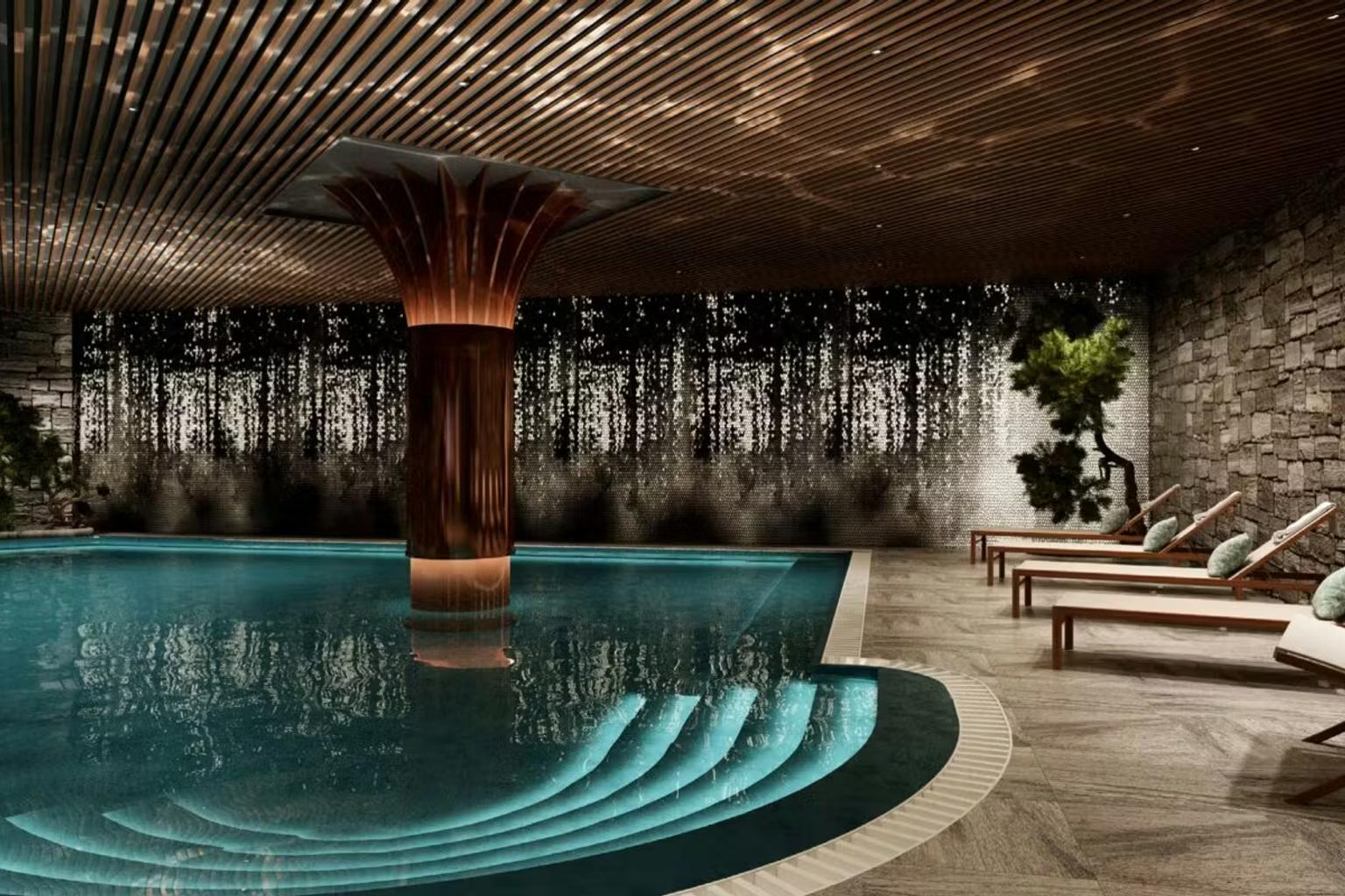 Moderne indendørs swimmingpool med en central kobbersøjle, oplyste trin, stenvægge, et skovmaleri og liggestole.