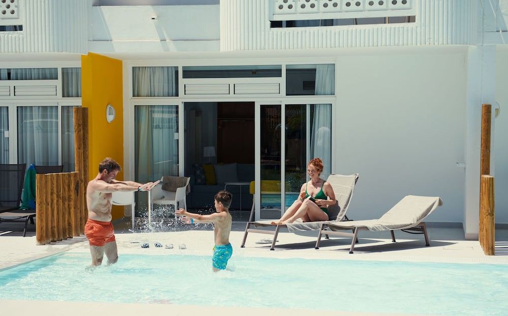 En familie nyder deres private pool; far og søn plasker, mens mor slapper af på en liggestol.