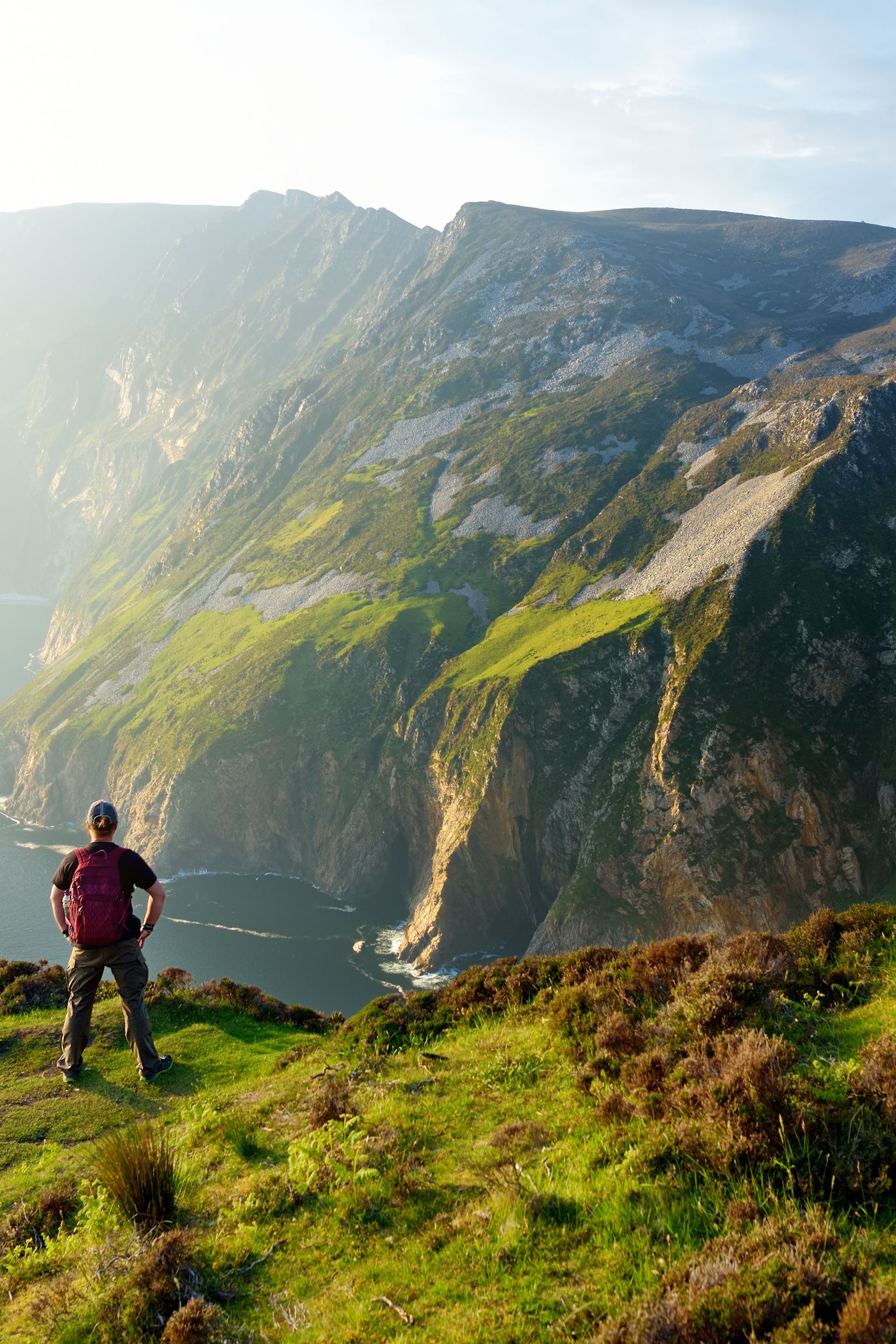 Person on a grassy cliff overlooking a vast ocean and dramatic sea cliffs.