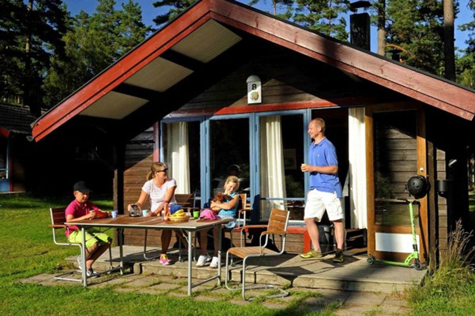 en familj sitter vid ett bord utanför ett litet hus