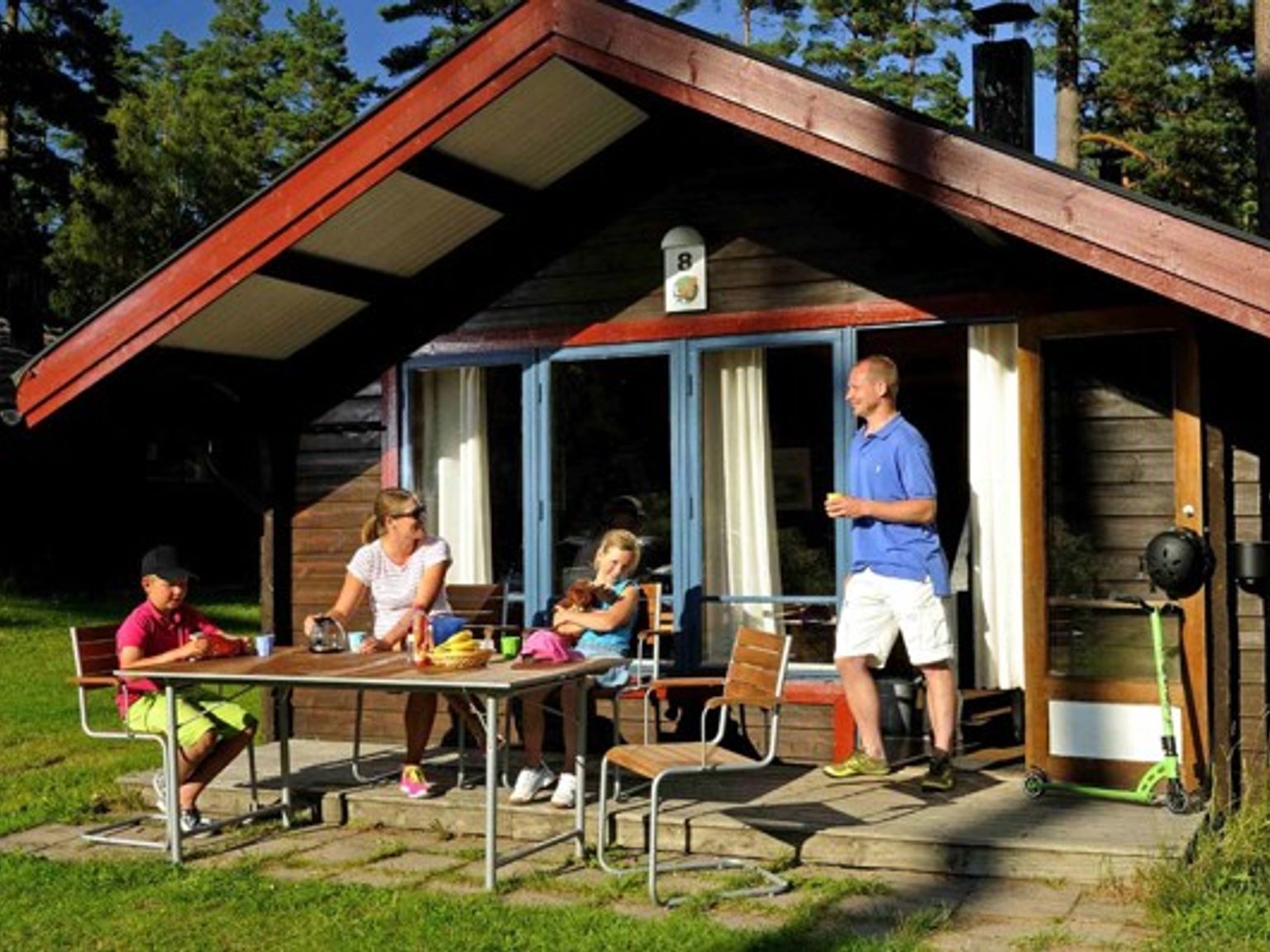 en familie sitter ved et bord utenfor et lite hus