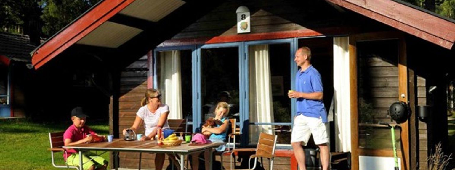en familie sitter ved et bord utenfor et lite hus