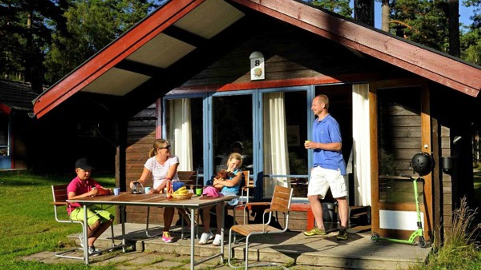 en familj sitter vid ett bord utanför ett litet hus
