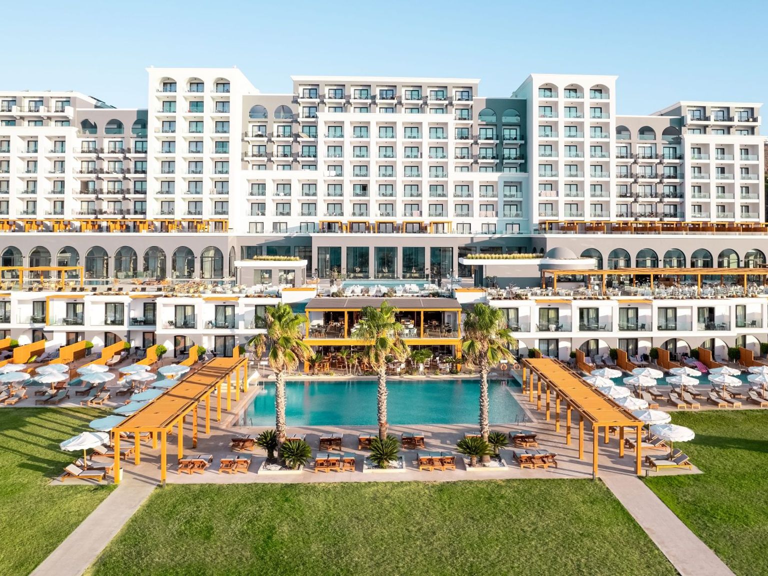 Duży, wielopiętrowy ośrodek z wieloma basenami, zielonymi trawnikami i rzędami leżaków. Mitsis Selection Alila