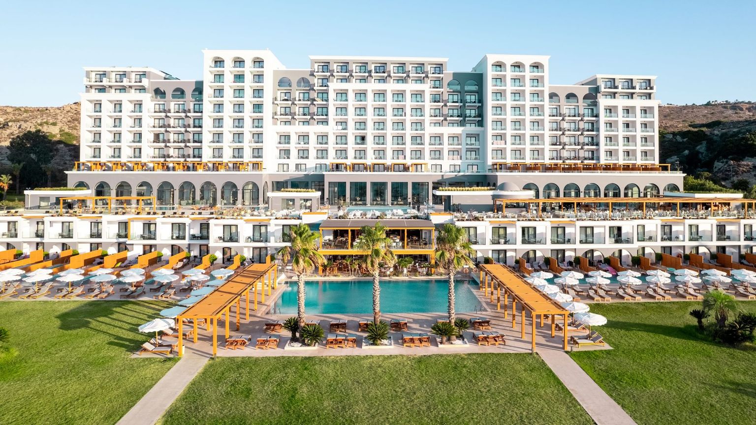 Et stort, fleretasjes feriested med flere svømmebassenger, grønne plener og rekker med solsenger. Mitsis Selection Alila