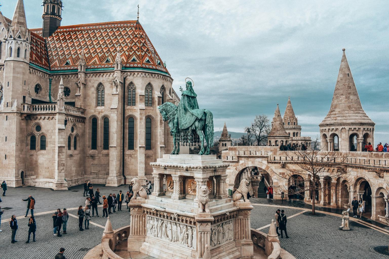 en statue av en mann som rir på en hest foran en stor bygning i Budapest.