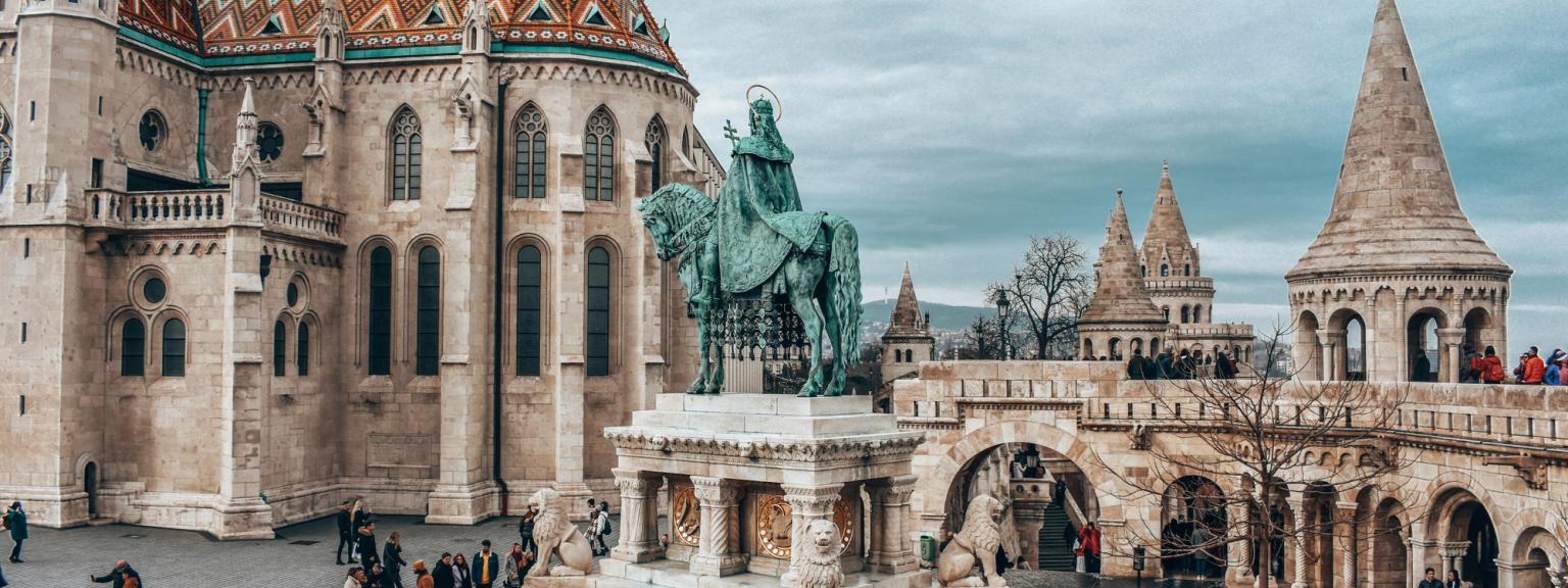 en staty av en man som rider på en häst framför en stor byggnad i Budapest.