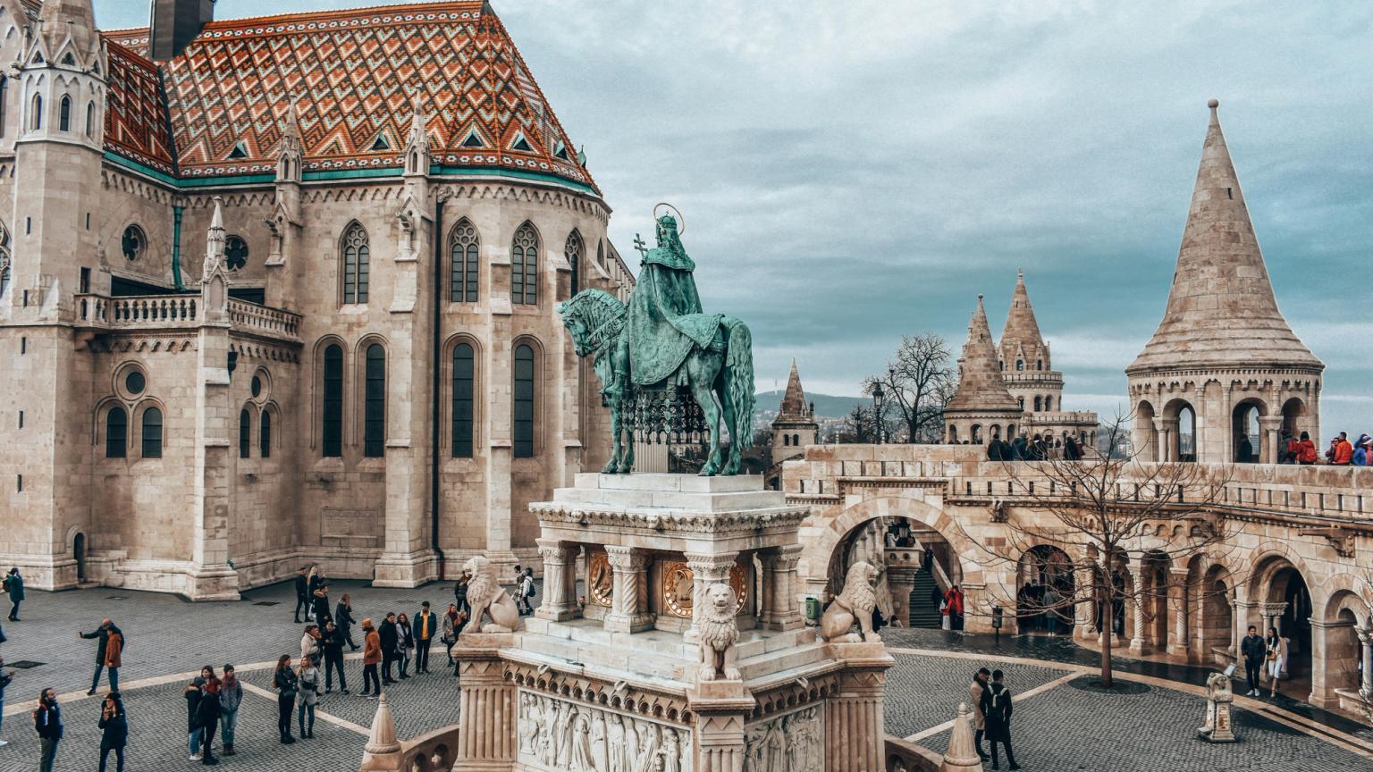 en statue av en mann som rir på en hest foran en stor bygning i Budapest.