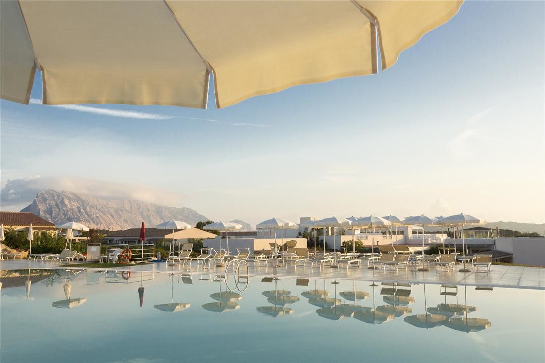 en stor swimmingpool omgiven av parasoller och stolar med berg i bakgrunden, Grande Baia Resort, Sardinien