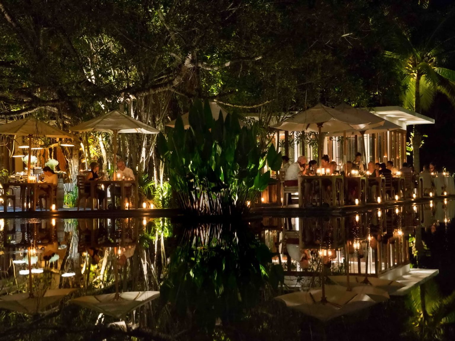 a group of people are sitting at tables outside of a restaurant at night.