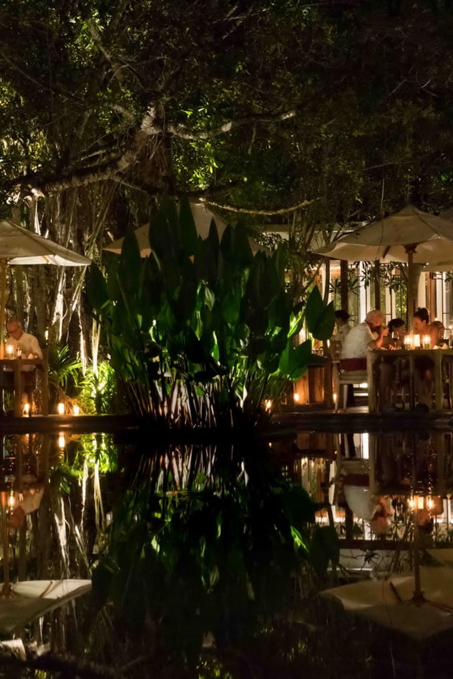 a group of people are sitting at tables outside of a restaurant at night.