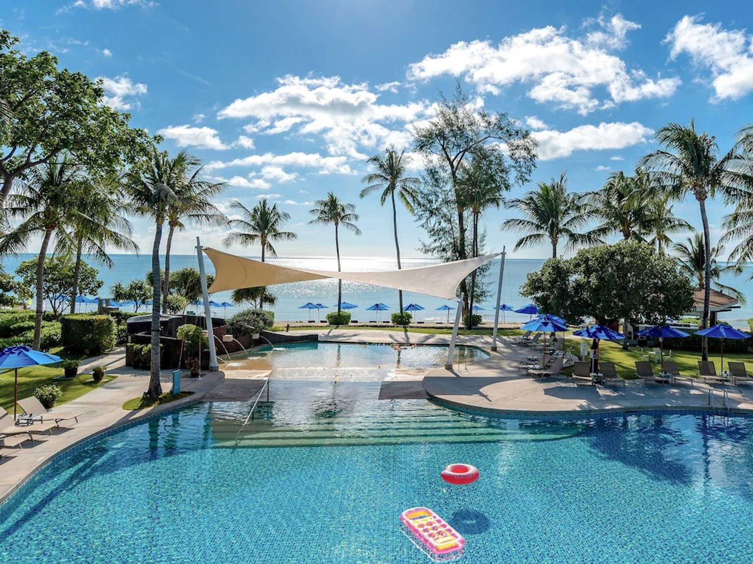 et stort svømmebasseng omgitt av palmetrær og paraplyer ved siden av havet