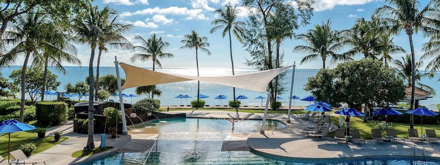et stort svømmebasseng omgitt av palmetrær og paraplyer ved siden av havet