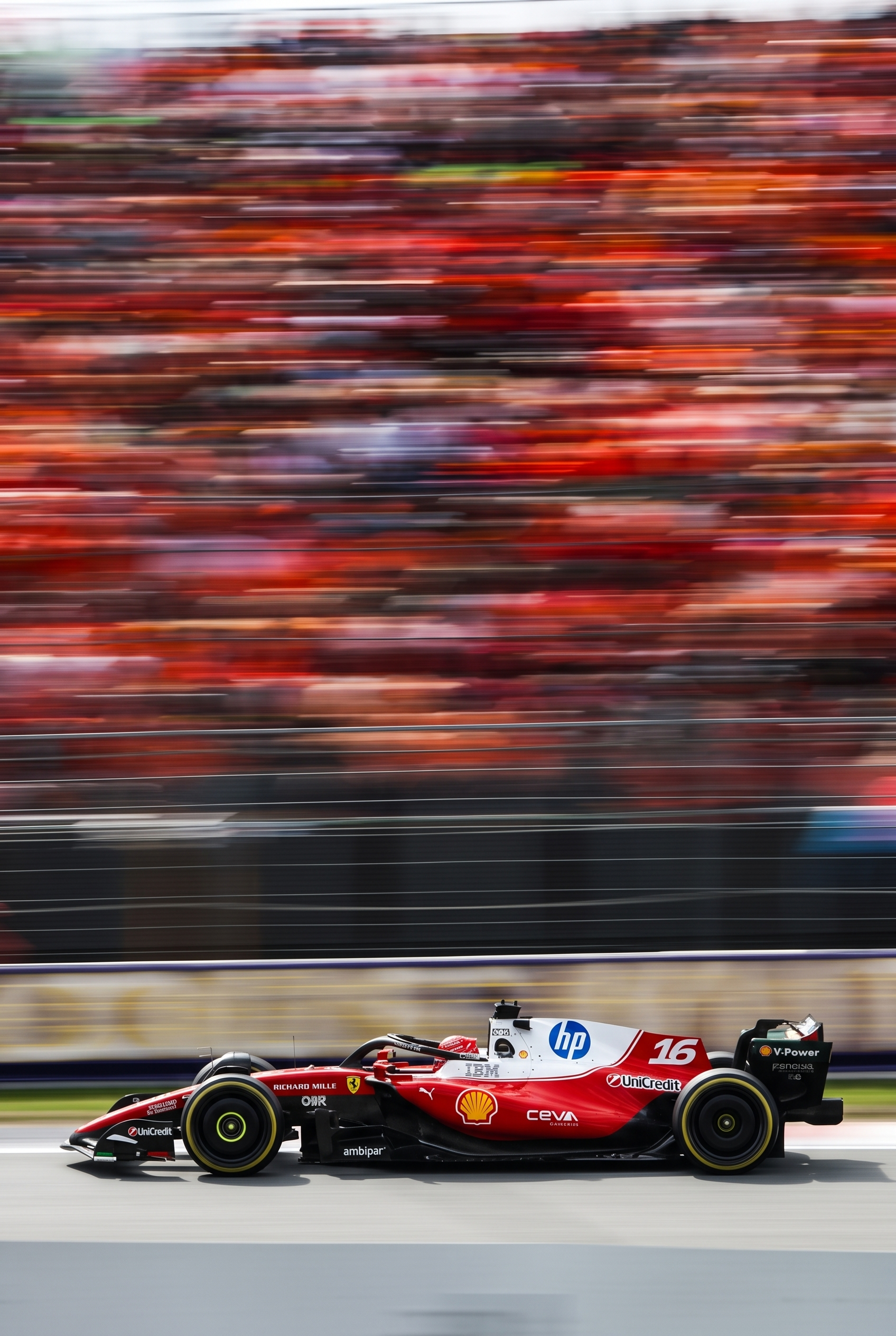 Voiture de F1 rouge et blanche numéro 16 passant à toute vitesse devant une foule floue.