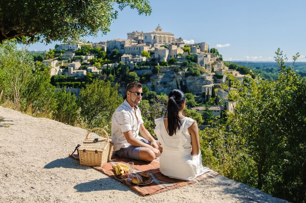 A couple having a picnic and enjoying the view of a scenic hilltop village. Gordes Luberon Provence.
