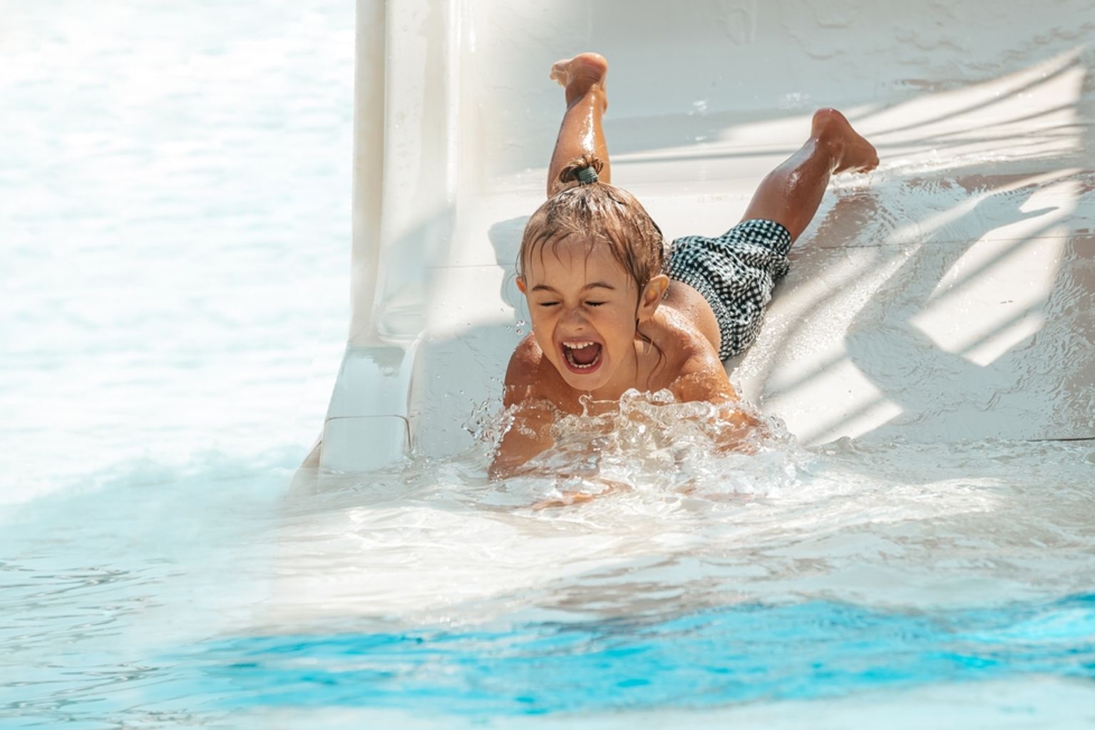 Ett glatt barn plaskar ut från en vattenrutschkana ner i en pool.