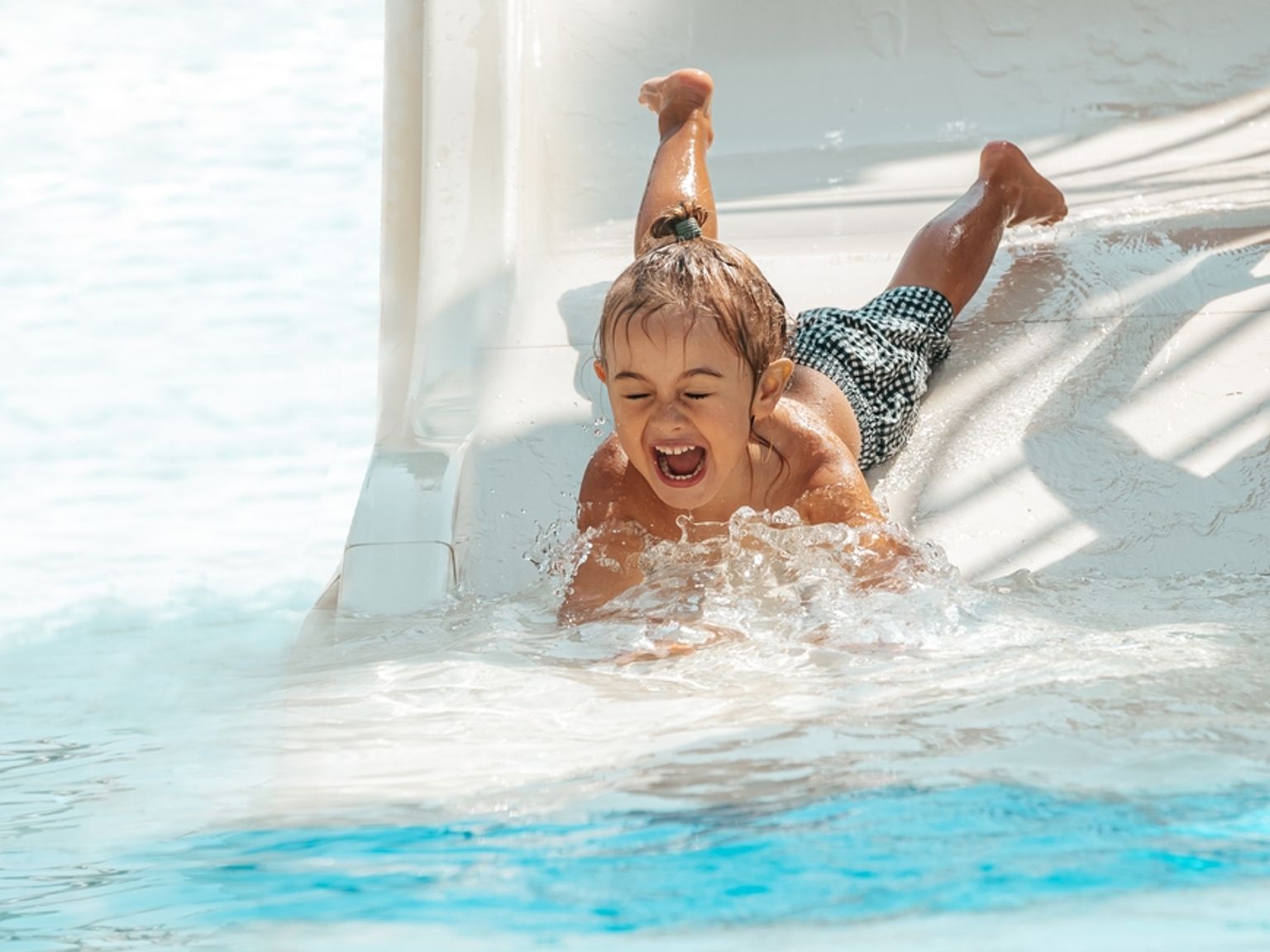 Ett glatt barn plaskar ut från en vattenrutschkana ner i en pool.