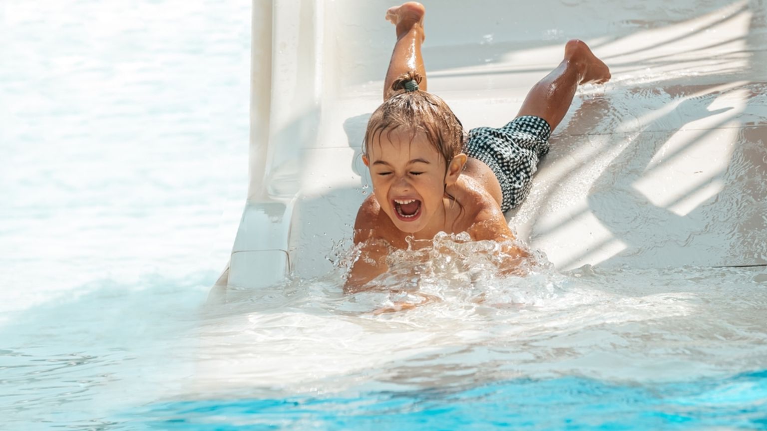 Ett glatt barn plaskar ut från en vattenrutschkana ner i en pool.