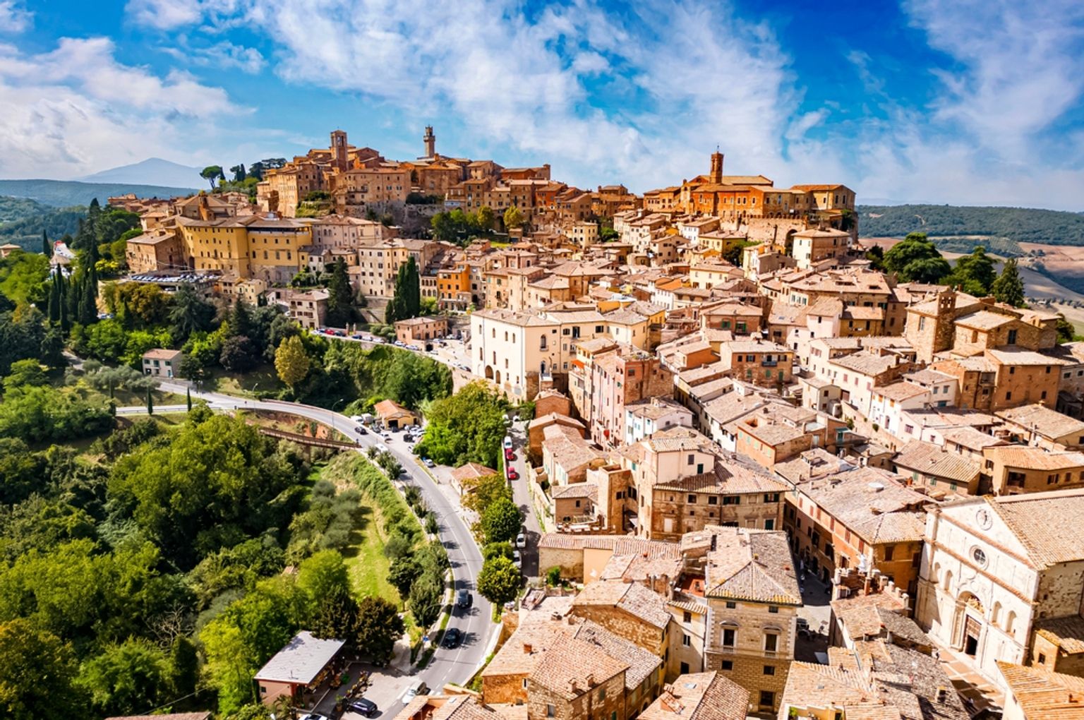 en flygvy över en liten stad i Italien omgiven av träd och berg.