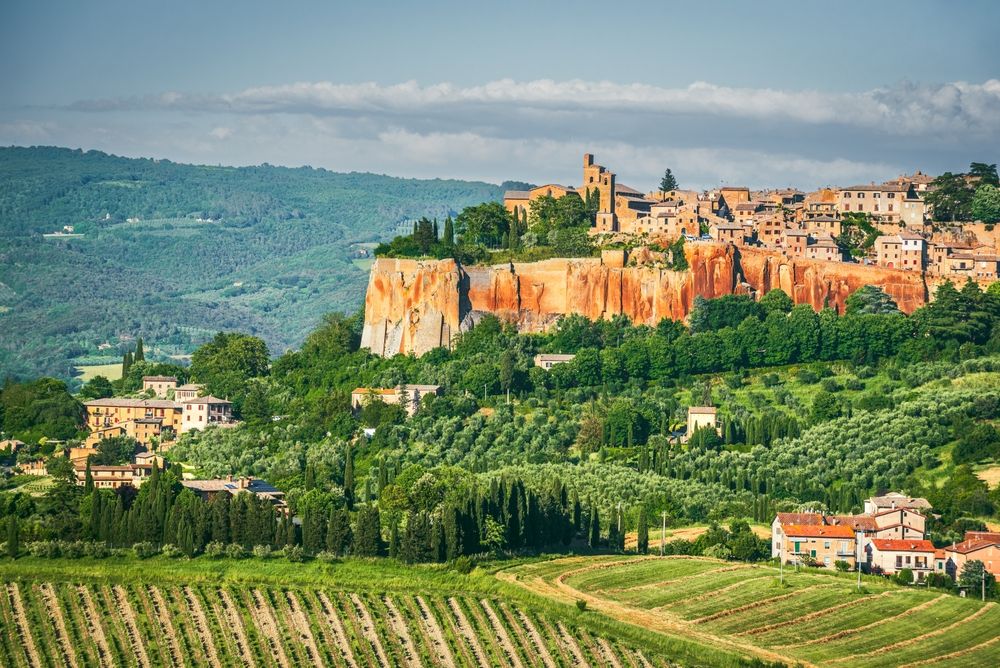 Historisk bakketoppby på en stor klippe med utsikt over grønne daler med vingårder og olivenlunder. Orvieto, Italia