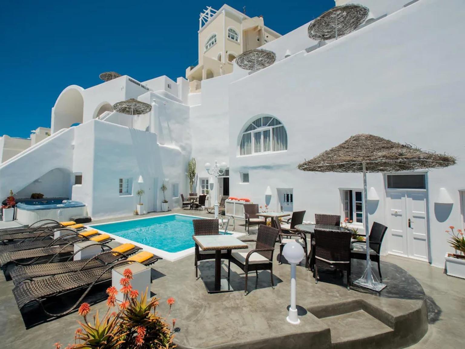 en stor hvit bygning med et svømmebasseng og bord og stoler foran.