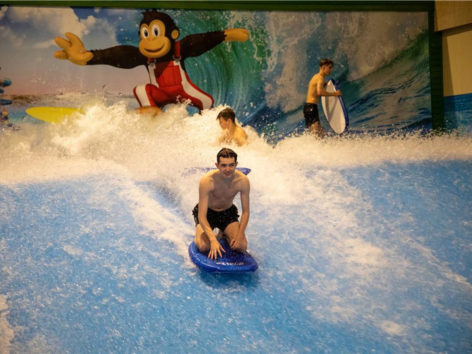En ung mand knæler på et boogiebræt og rider på en kunstig bølge i en vandpark. Lalandia Resort Søndervig