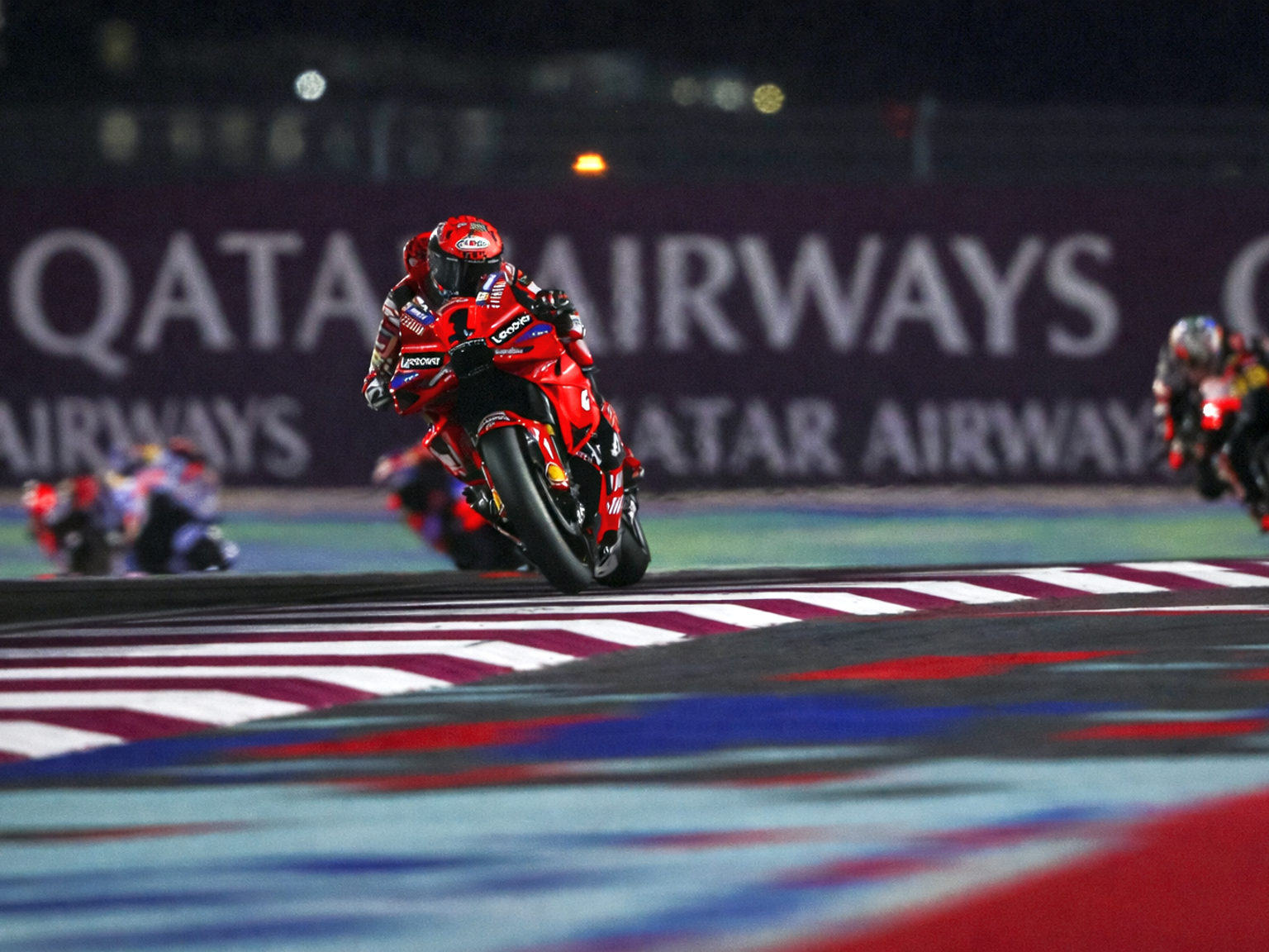 Punainen moottoripyöräkilpailija kallistuu mutkaan radalla yöllä, taustalla näkyy "QATAR AIRWAYS".