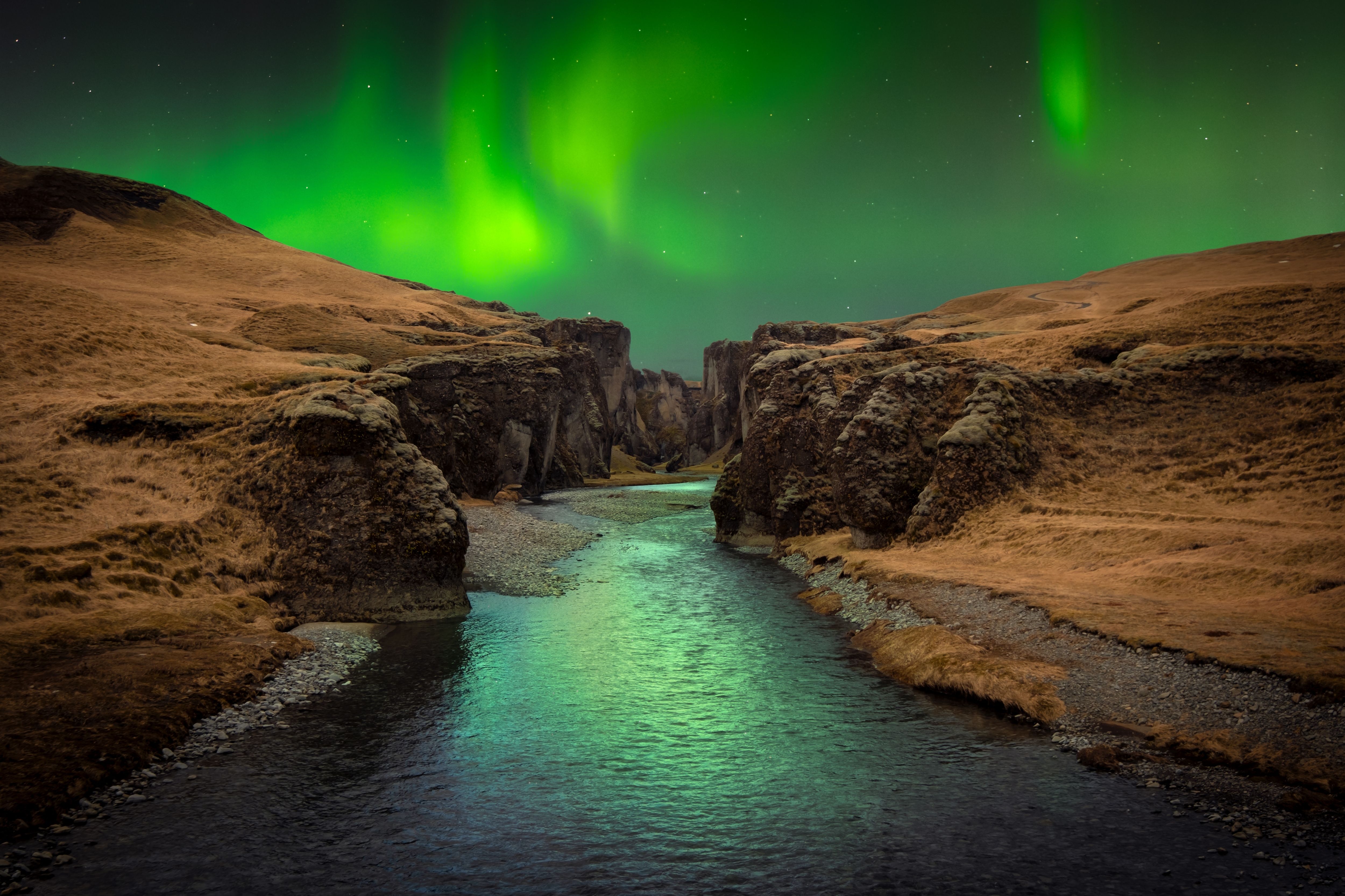 the aurora borealis is shining over a river in the middle of a canyon