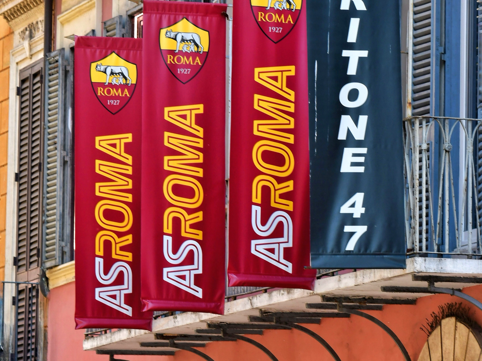 Røde AS Roma-bannere og et svart Tritone 47-banner henger fra en bygning over et AS Roma Store-skilt.