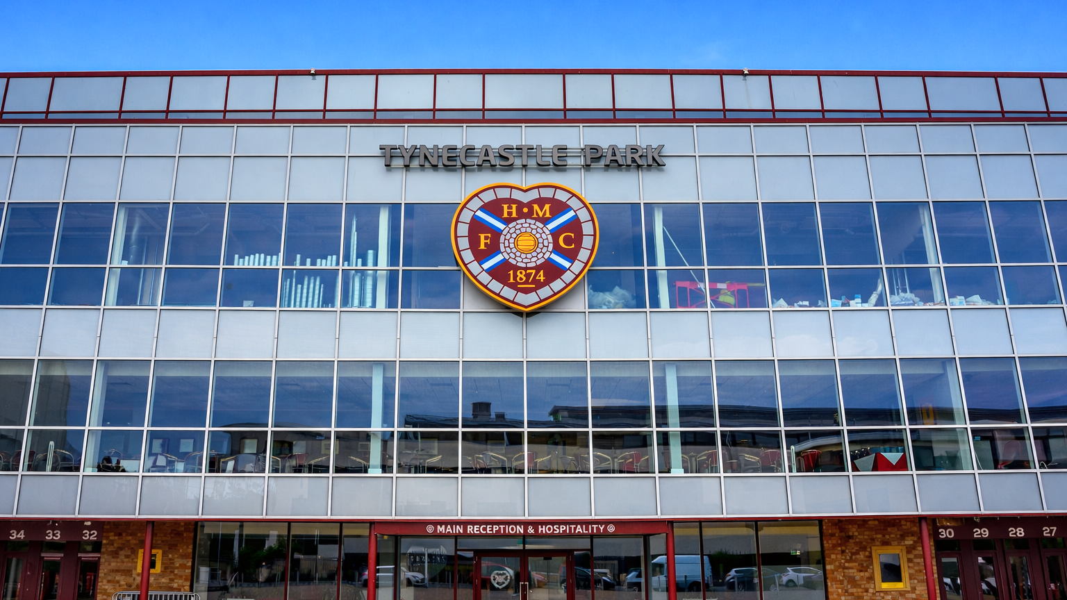 Exterior of Tynecastle Park stadium with the Heart of Midlothian FC crest on its glass facade.