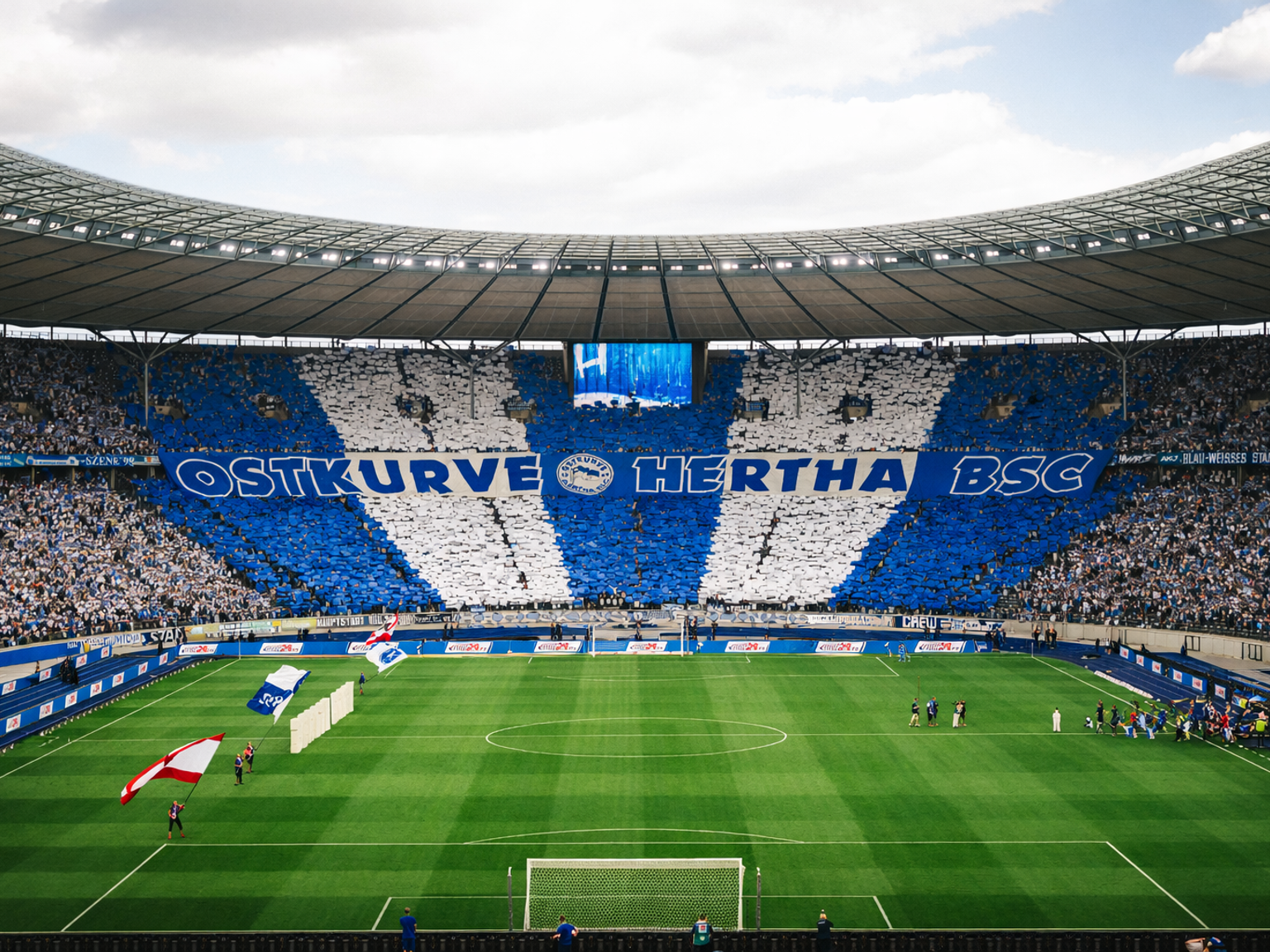 Fans in einem großen Fußballstadion zeigen ein blau-weißes Tifo mit der Aufschrift 'OSTKURVE HERTHA BSC'.