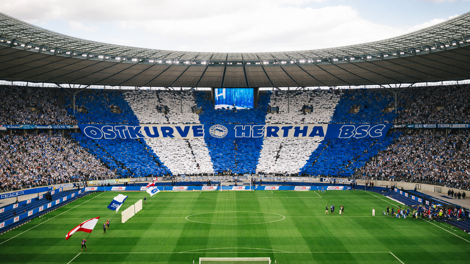 Aficionados en un gran estadio de fútbol muestran un tifo azul y blanco que deletrea 'OSTKURVE HERTHA BSC'.