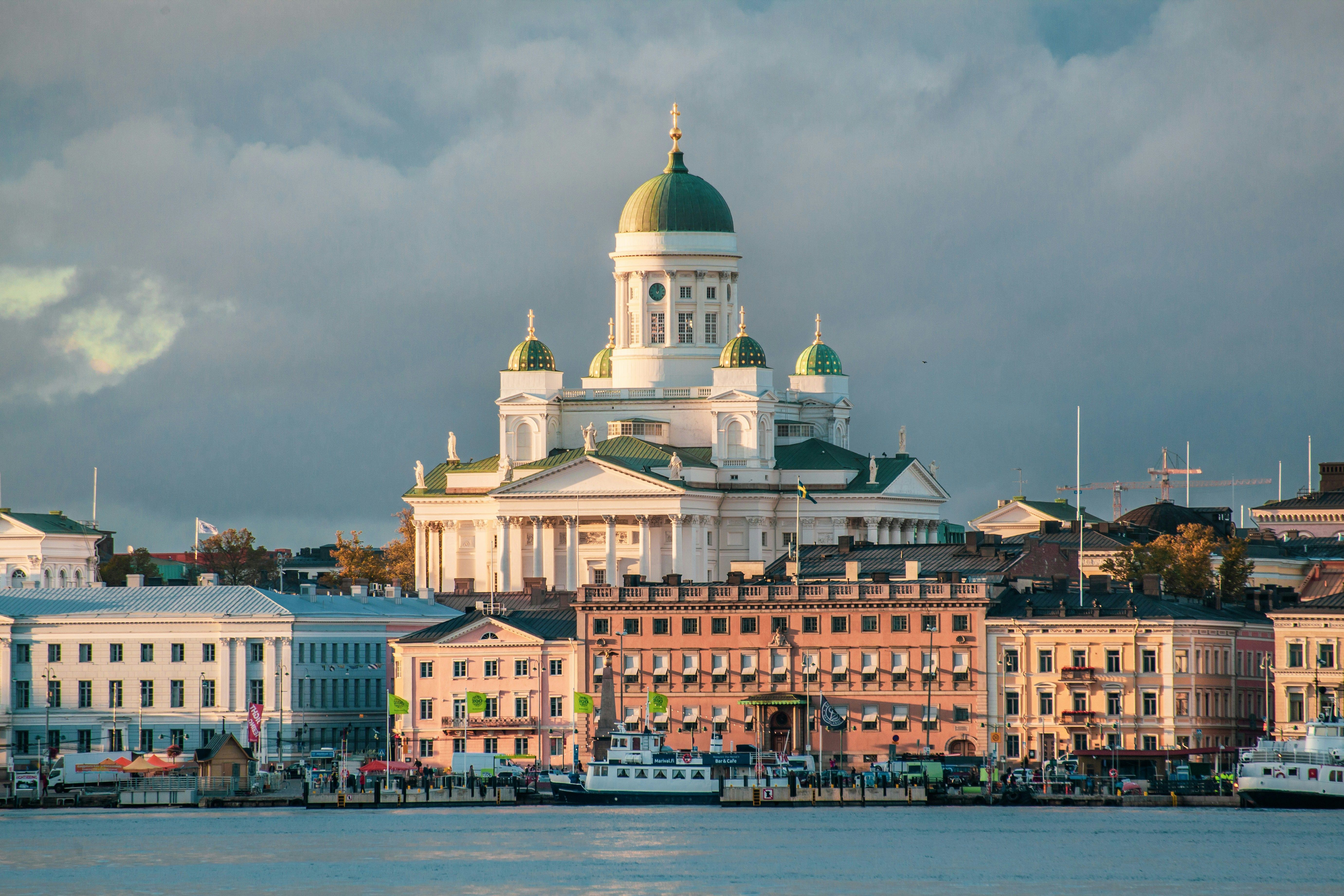Helsingfors domkirke med sine grønne kupler med utsikt over en fargerik havneby med båter.