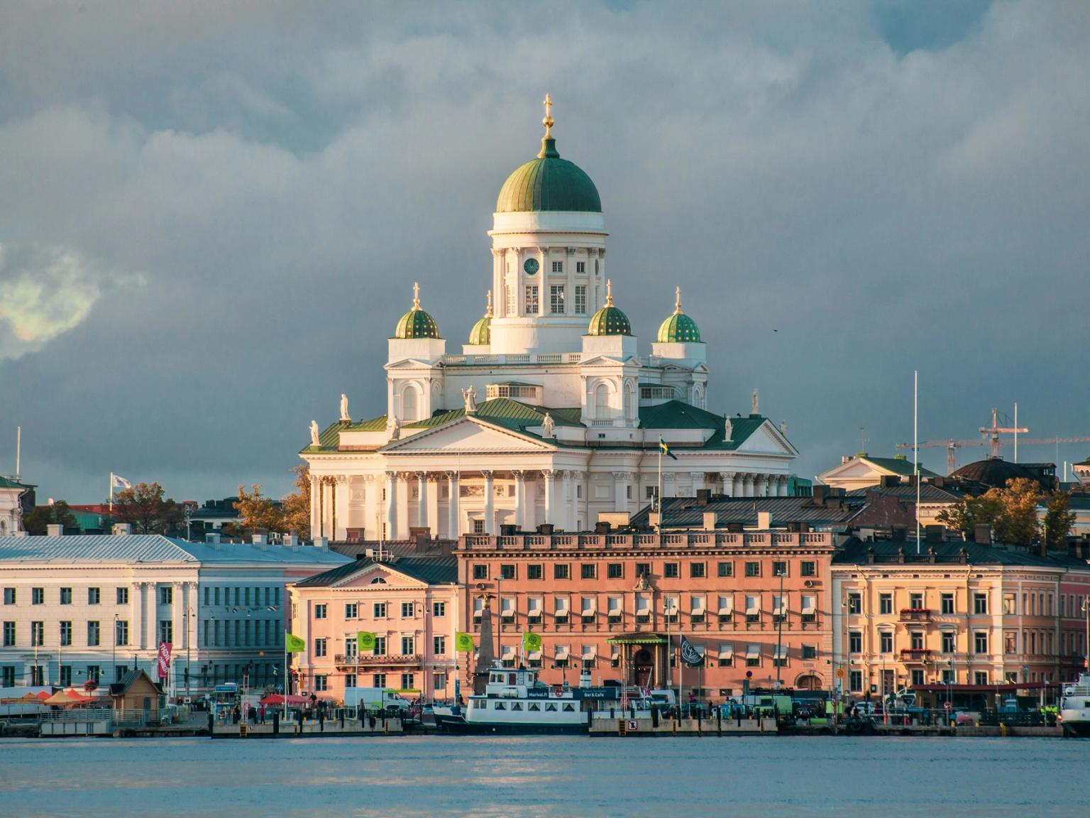 Helsingfors domkirke med sine grønne kupler med utsikt over en fargerik havneby med båter.