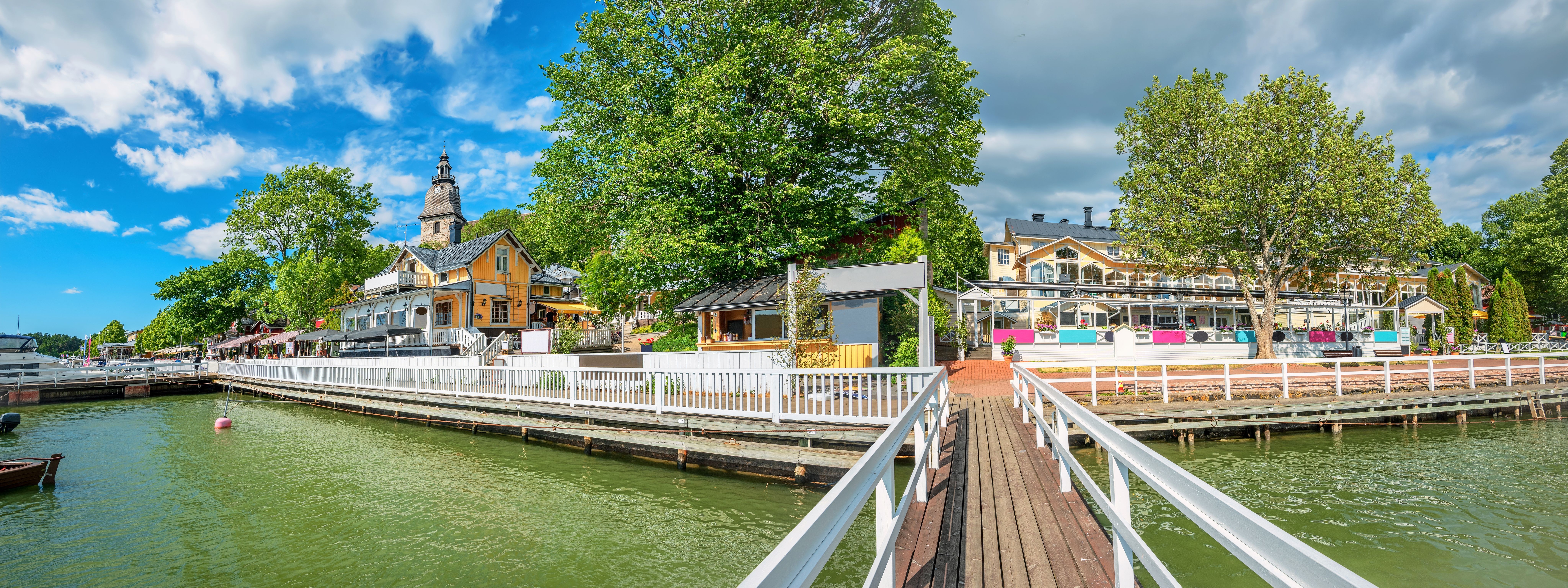 Panoramisk udsigt over en livlig by ved vandet med et kirketårn og en mole.