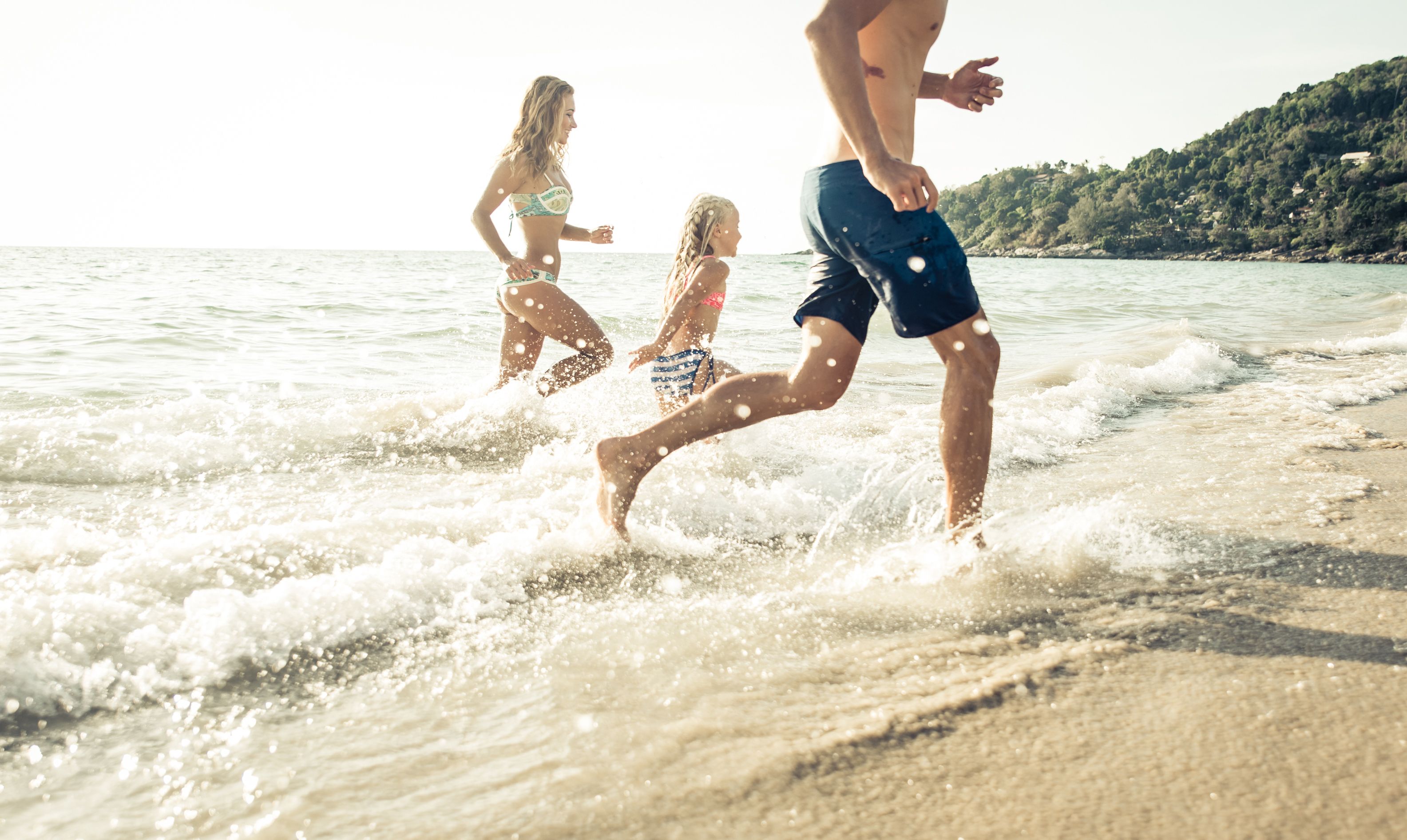 En familj springer genom grunda vågor på en solig strand.