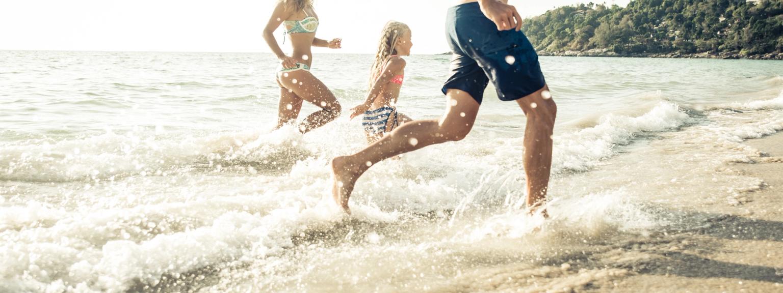 En familj springer genom grunda vågor på en solig strand.